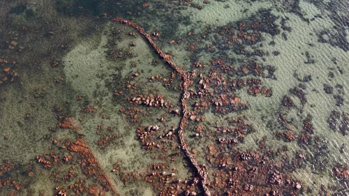 an aerial shot of a coastline with a line of rocks through the center of the water
