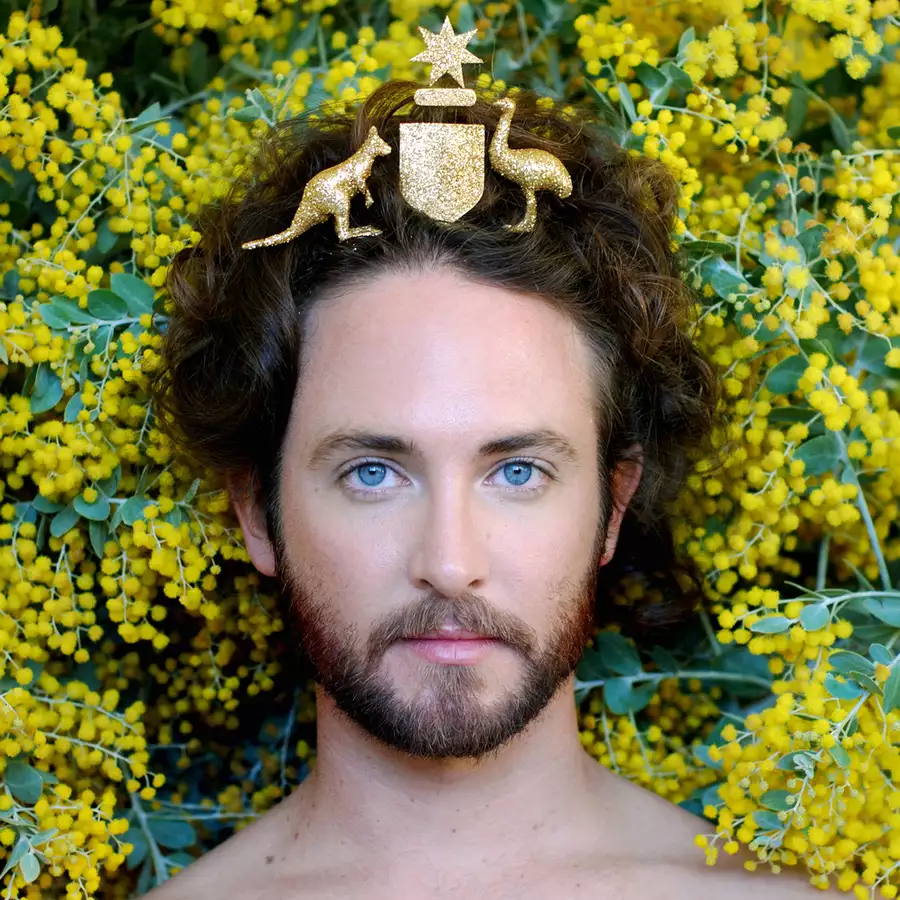 an image of artist Liam Benson with the Australian coat of arms on his head with yellow wattle behind him