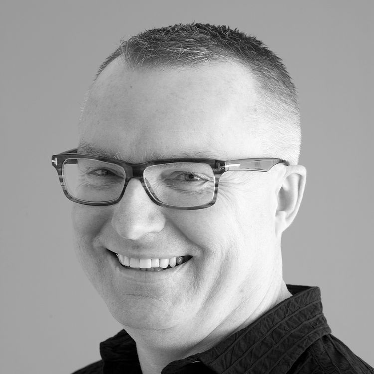 Black and white close up photo of a man with no beard and glasses, smiling