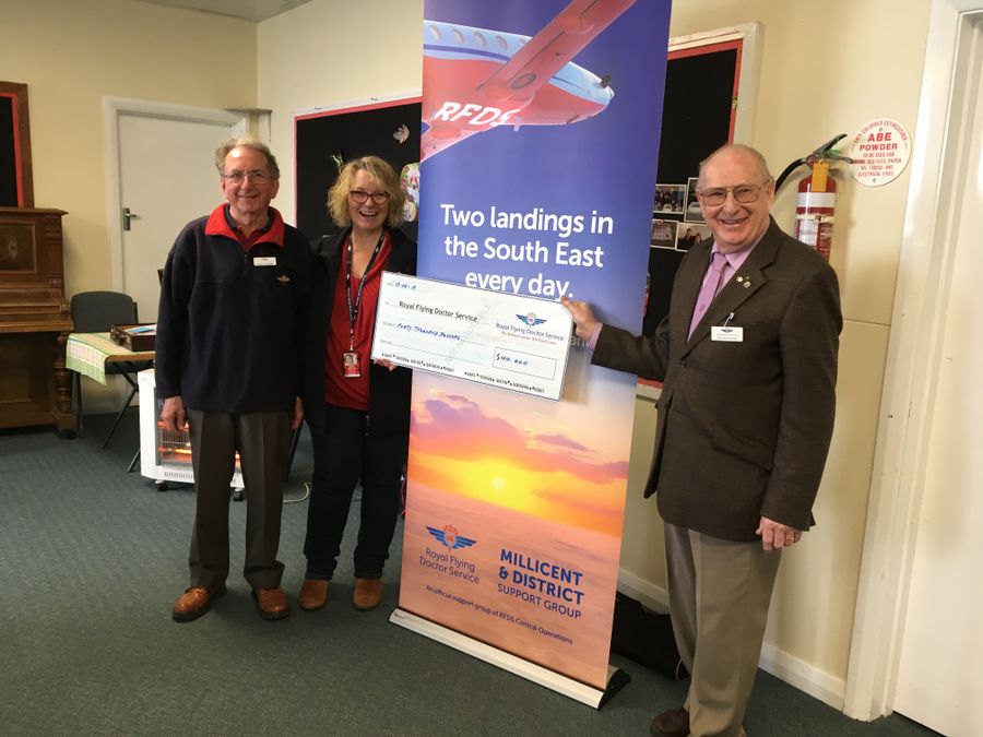 Three people smile at the camera. They are holding an oversized cheque for $40,000 made out to the RFDS. 