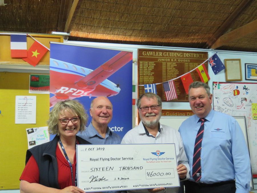A group of people holding an oversized cheque smile at the camera. They are standing in front of a RFDS aircraft.