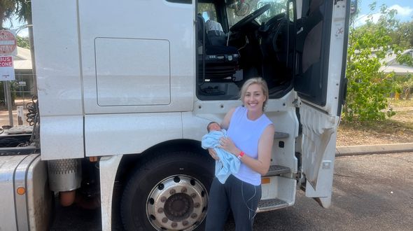 Ella holding baby Lucas in front of prime mover truck.
