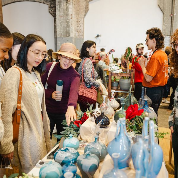 A group of people looking at ceramics on a market table with lots of other attendees in the background