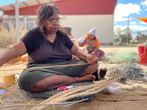 A woman threads a needle for a woven art piece