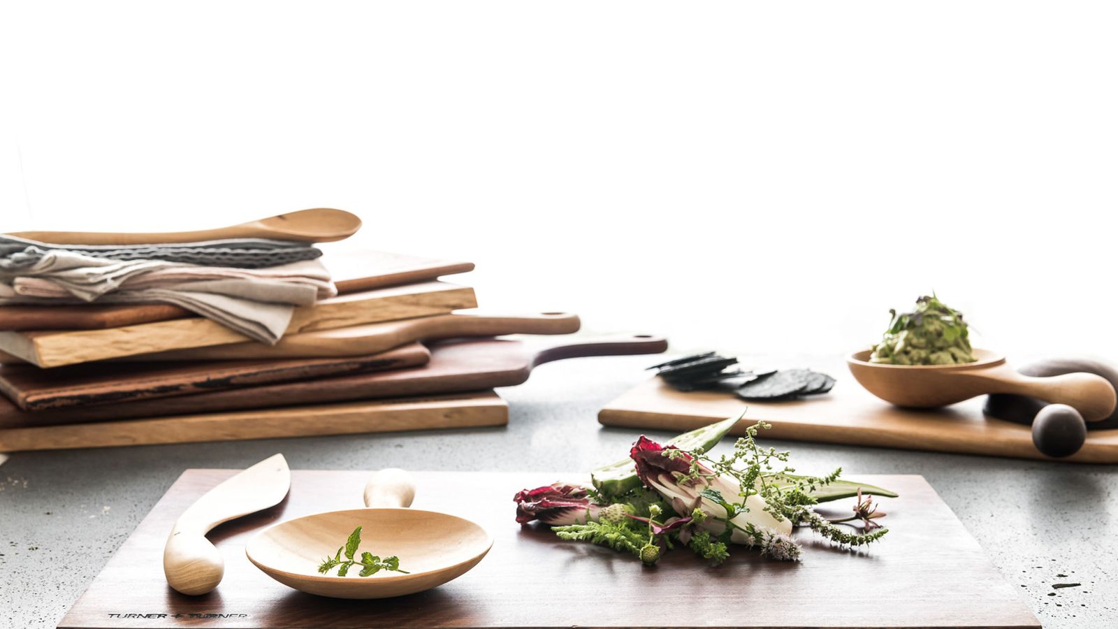A stack of wooden chopping boards, plus some wooden utensils arranged on a table.