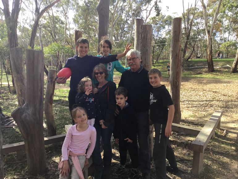 Two adults and five children are outdoors smiling at the camera. 