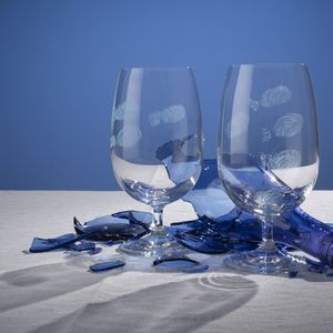Two wine glasses with engraved fingerprints and a shattered blue glass bottle