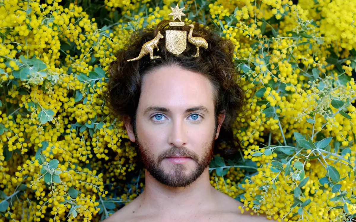 an image of artist Liam Benson with the Australian coat of arms on his head with yellow wattle behind him