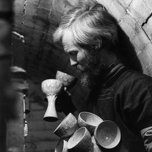 Photo of a man with a beard holding a bunch of ceramic goblets side view in black and white.