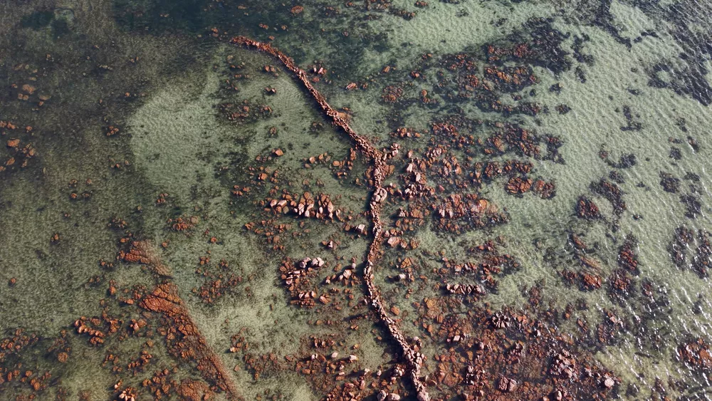 an aerial shot of a coastline with a line of rocks through the center of the water