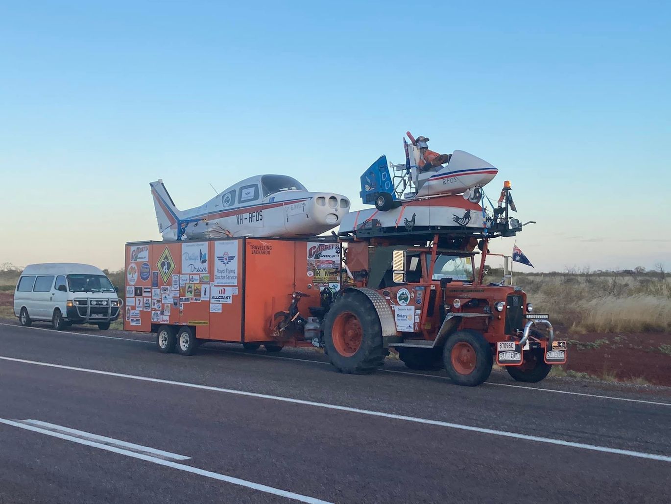 An orange tractor tows an orange box with the an aircraft replica on top.