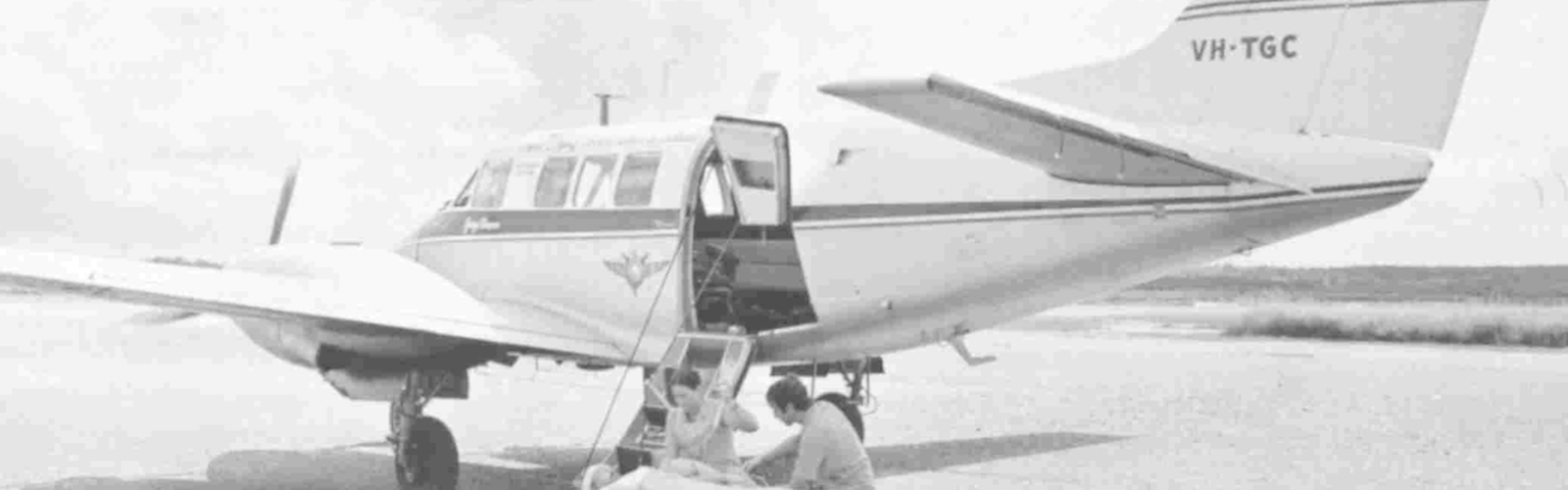 A black and white photo showing an old RFDS aircraft with a doctor tending to a patient in the foreground