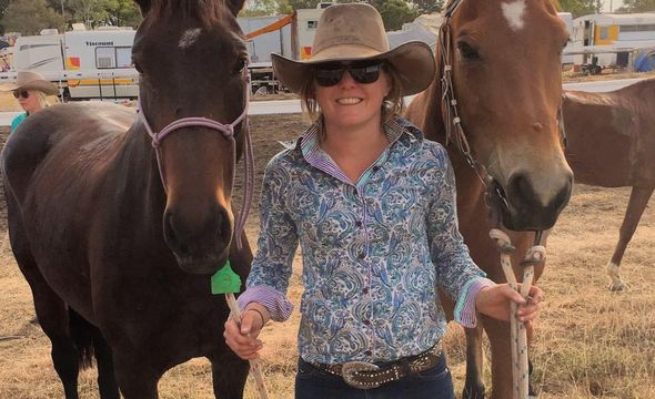 A young woman smiles. She is standing next to two horses.