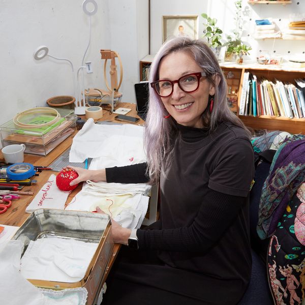 Photo of Sue Jo Wright at her desk in her studio with some textile work in progress pieces on the desk