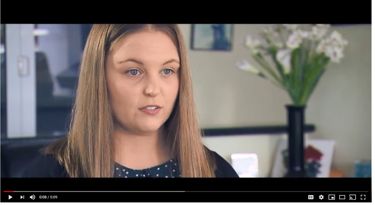 A YouTube screen showing a young woman with straight shoulder length hair. She appears to be mid-sentence.