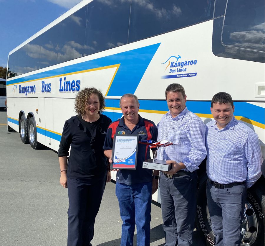 six people standing in front of a Kangaroo Bus Lines bus holding a Royal Flying Doctor Service model plane 
