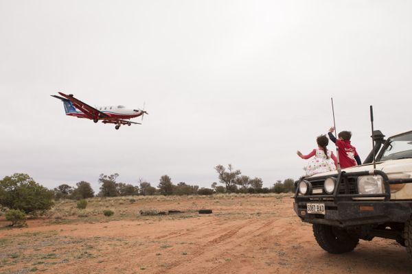 An aircraft with RFDS logo flies over green paddocks. 