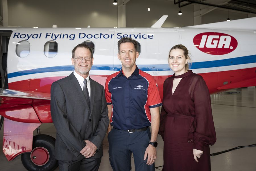 4 people in business attire smile at the camera. There is a RFDS aircraft in the background.