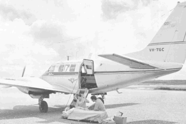A black and white photo showing an old RFDS aircraft with a doctor tending to a patient in the foreground