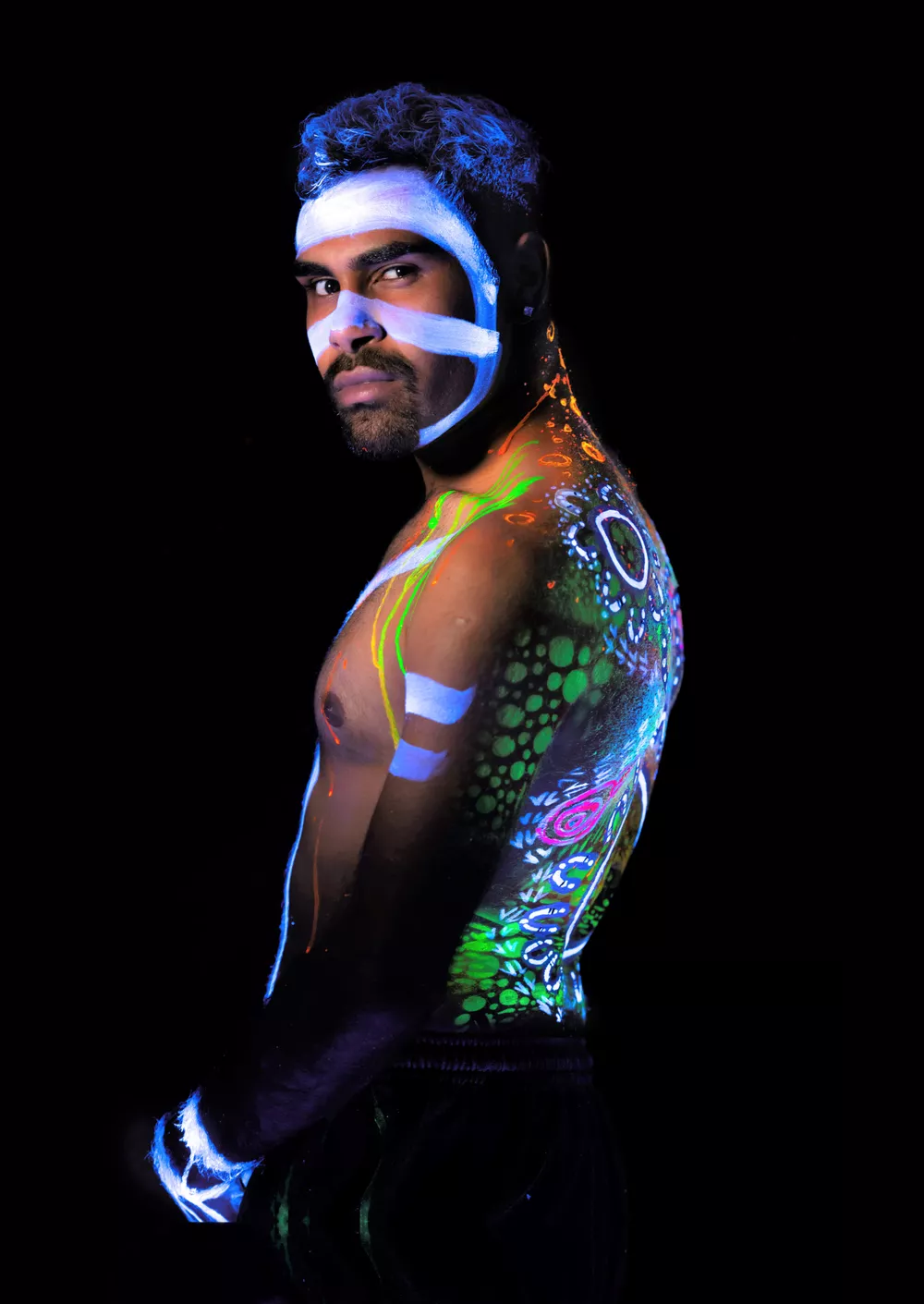 A First Nations man poses with UV paint covering him