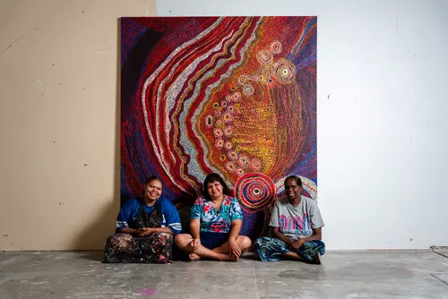 Three women sit in front of a painting