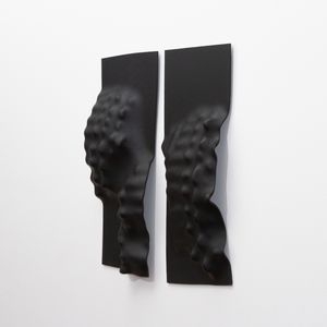 Two black rectangular pieces of glass with wavy, textured surfaces hang vertically on a white wall.