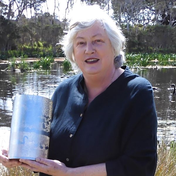 Photo of a woman with a grey bob standing in front of a pond of swans.