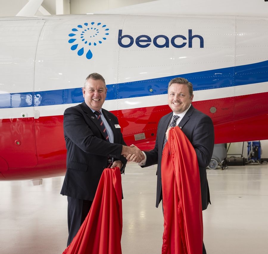 Two men wearing suits shake hands. They are standing in front of an aircraft with a BEACH Energy logo on the side. 