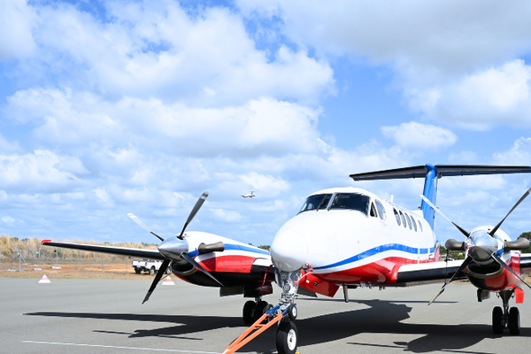 RFDS aircraft on Bundaberg airport tarmac with another RFDS aircraft in sky 