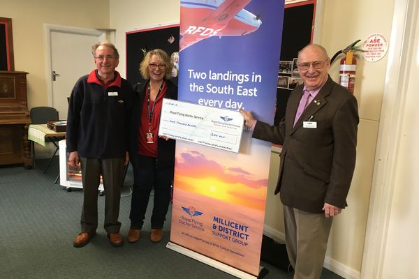 Three people are smiling at the camera and holding an oversized cheque for $40,000 made out to the RFDS. They are standing in front of a RFDS banner. 