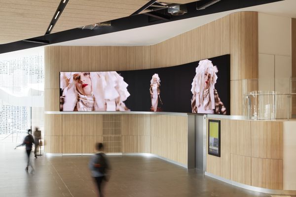 A photograph of a wide digital screen in a foyer with a woman in a headdress on the screen.