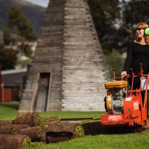 A photo of Kirsha Kaechele taking up the lawn at MONA with a turf cutter
