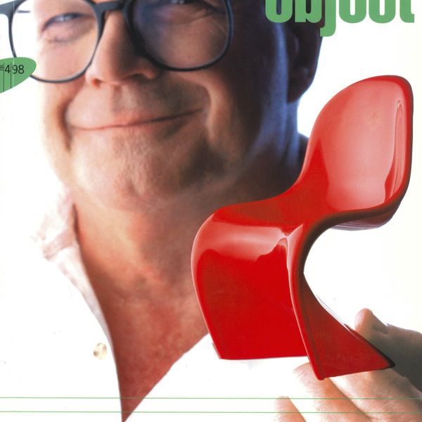 A colourful magazine cover. A shiny red plastic designer chair is positioned in the foreground and the face of a smiling man wearing glassed is placed in the background.