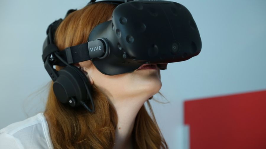 Close up photograph of a female with long red hair wearing a black virtual reality headset. 