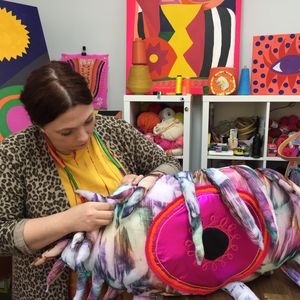 Female in vibrant studio space stitching a large soft sculpture in the shape of an eye