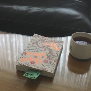 A book with a green bookmark are placed next to a cup of coffee on a table