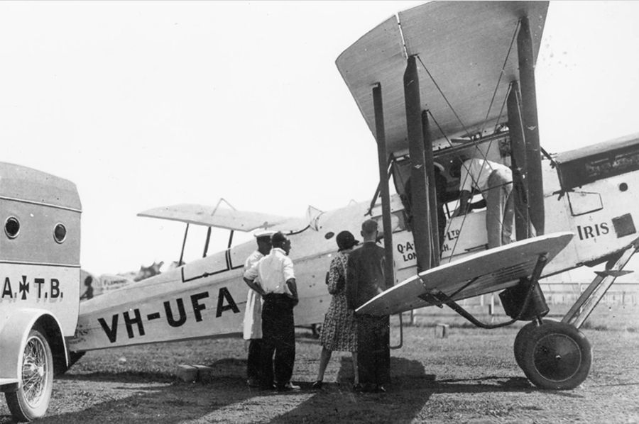 four people standing in front of a plane next to an ambulance, image is in black and white indicating it is from a long time ago