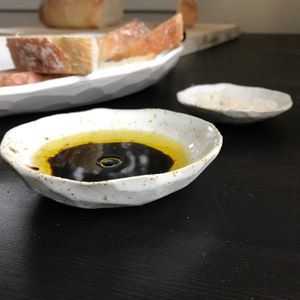 A small dish containing dipping oil, with a tray of crusty bread in the background.