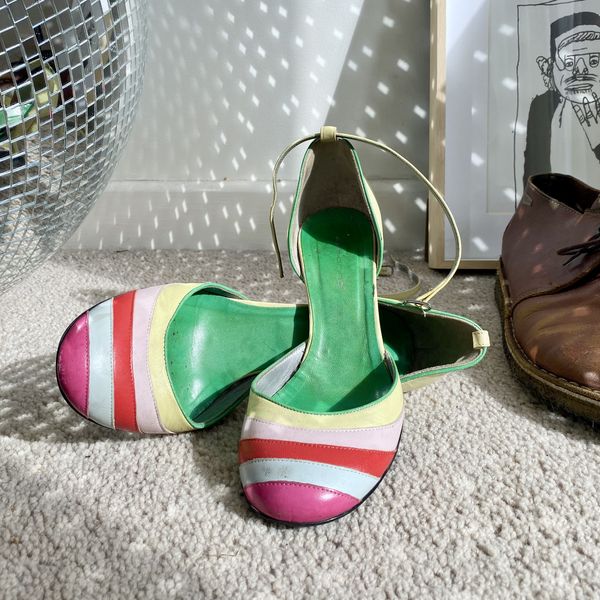 A pair of colourful high heels, A pair of brown leather boots, a disco ball and a framed drawing are grouped together on the floor