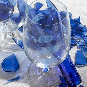 shattered blue glass bottle and clear glasses tumblers with engraved fingerprints on the surface