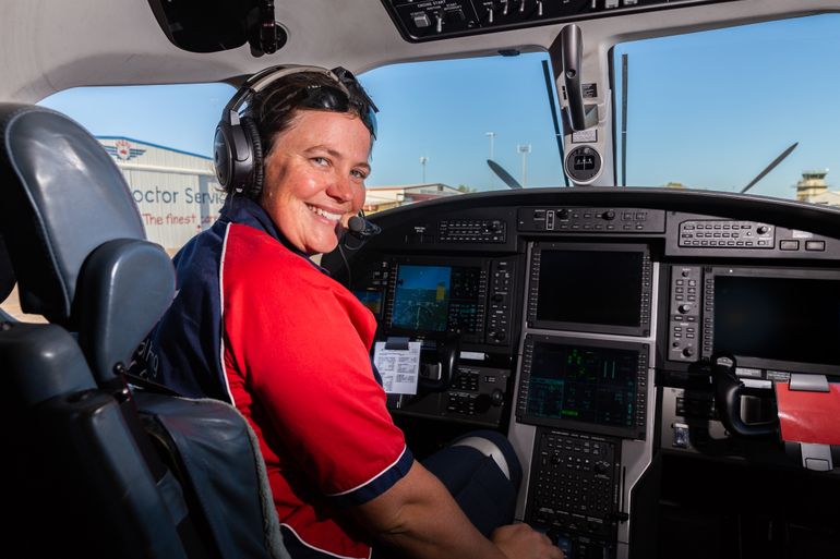 RFDS Pilot Heather Ford in the cockpit of a Pilatus PC12 aircraft. She is smiling and wearing a headset. 