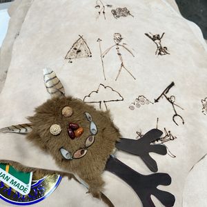 A kangaroo skin childrens cloak that is covered with children's drawings and has a furry monster toy on top