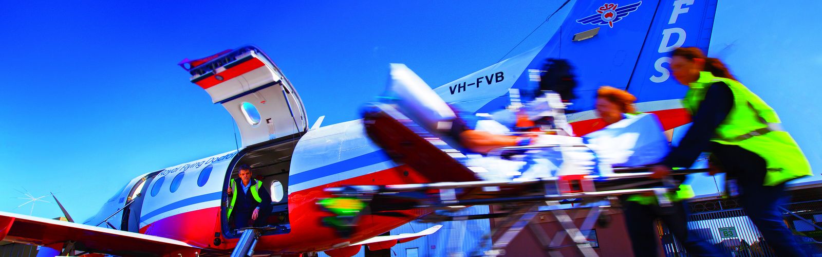 A person lying on a hospital stretcher is pushed toward an aircraft with RFDS logo. 