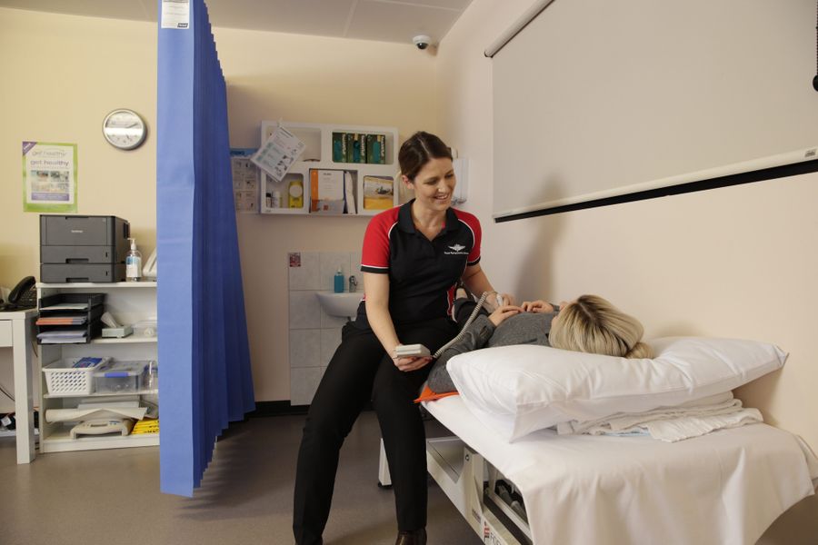 A pregnant woman lies on a hospital bed. A woman in a RFDS shirt sits beside her, feeling her tummy. 