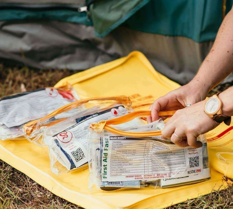 A yellow Rescue Swag is on the ground open displaying the first aid items inside.