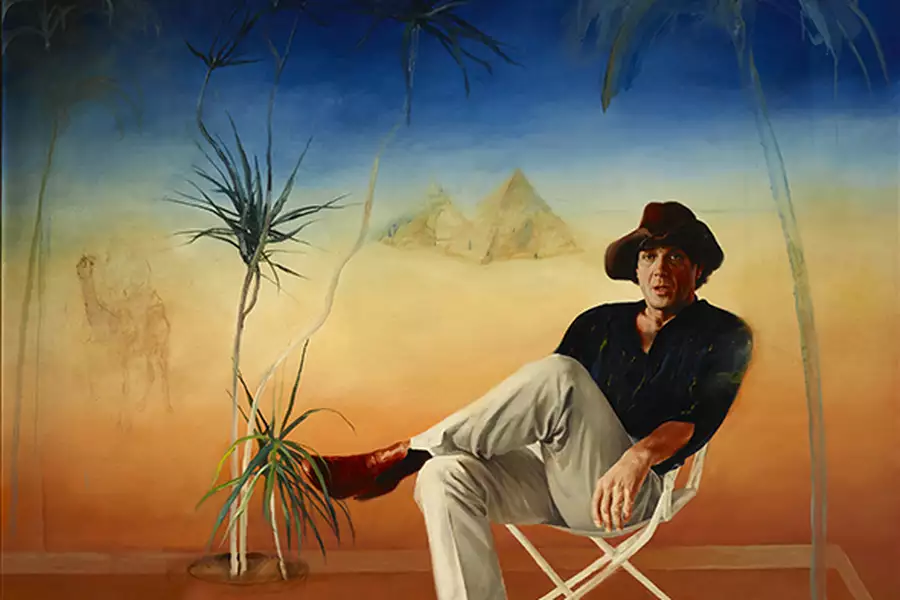 A painting of Molly Meldrum sitting on a white fold-out chair. The blue, yellow and brown background has palm trees and pyramids