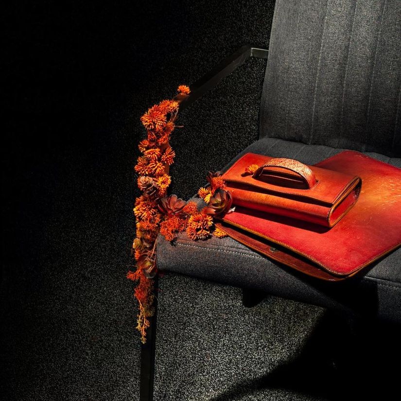 An orange leather handbag and satchel on a grey chair decorated with orange dried flowers