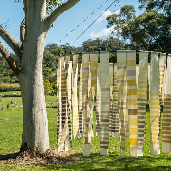 Backdrop of a country cemetry on a beautiful day with a hoop of naturally dyed lengths of fabric hanging from a large eucalyptus tree