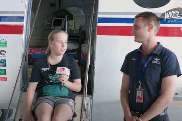 11 year old, Eliza, is pictured next to pilot, Elliot Johnston who is being interviewed. They are seated in front of an RFDS aeroplane, smiling.