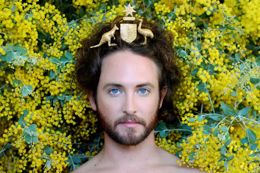 an image of artist Liam Benson with the Australian coat of arms on his head with yellow wattle behind him